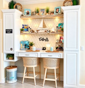 A coffee bar with a sign, a coffee machine, two wicker stools, and decorative items on shelves. - Coastal Comfort•On 30A•Between Rosemary Beach and Alys Beach•Three Bedroom• (Seacrest)