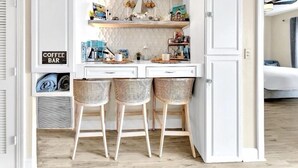 A compact kitchen with a coffee bar, two wicker stools, and a sign indicating a coffee bar. - Coastal Comfort,Spacious and Bright Condo right on 30A (Seacrest)