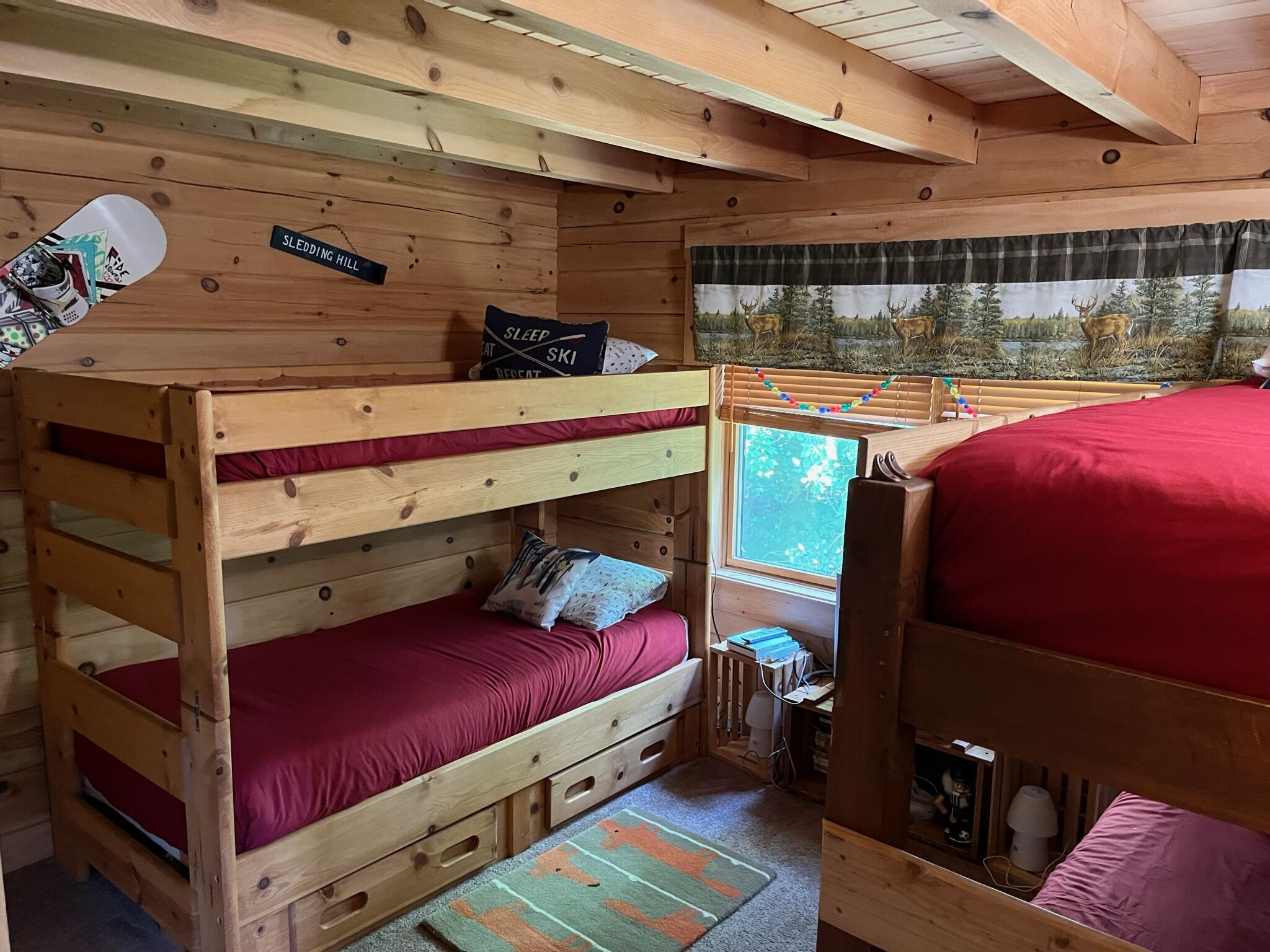 Ein Schlafraum mit Etagenbett, Fenster, rotem Bett und einem Kissen mit dem Aufdruck "SLEEP REPEAT SKI".