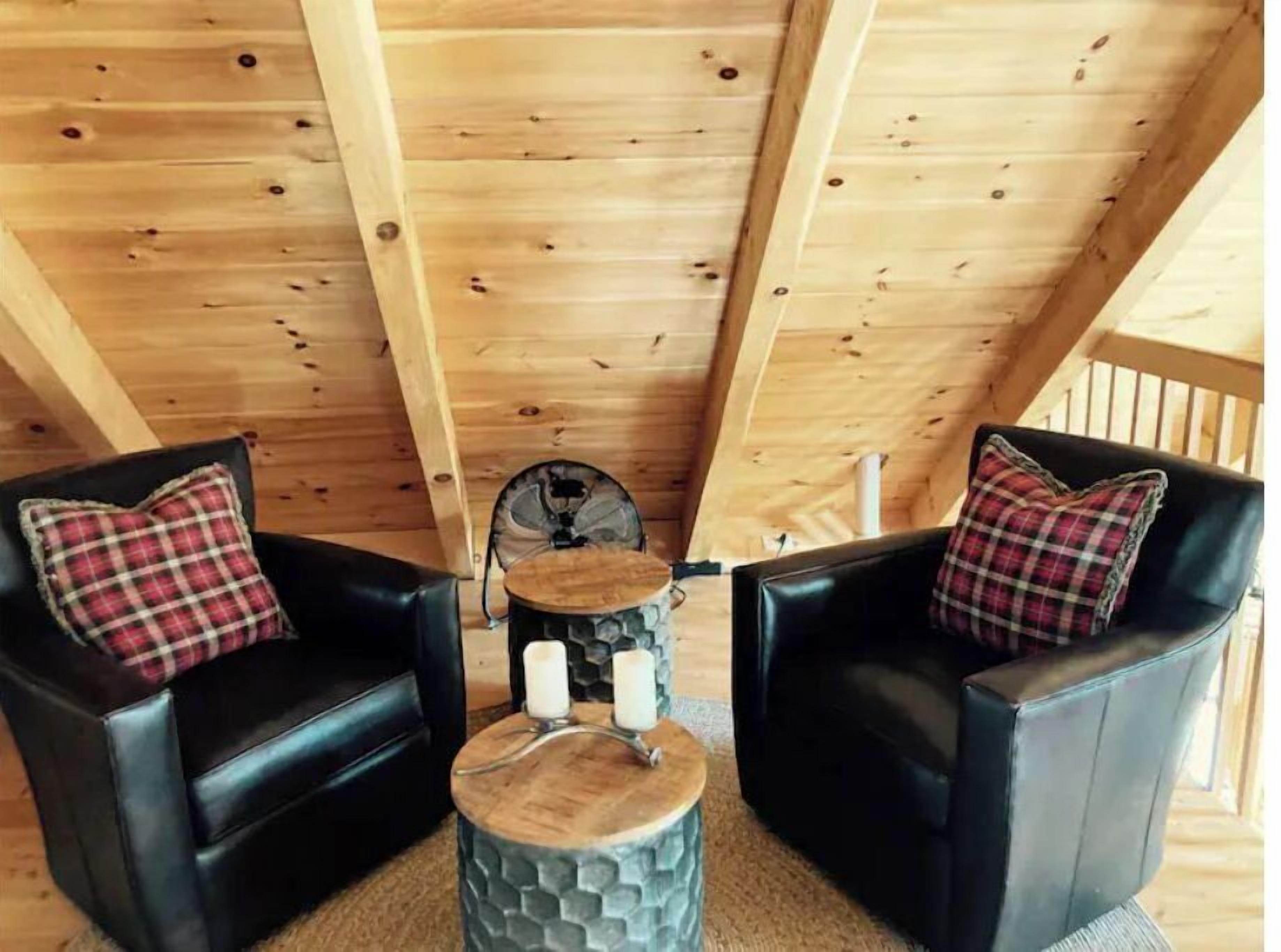 Una habitación acogedora con vigas de madera en el techo, dos sillones de cuero negro con cojines a cuadros y una pequeña mesa redonda con velas.