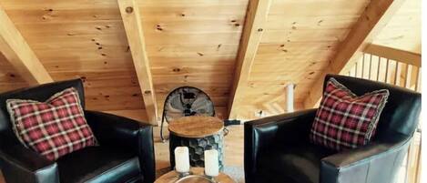 Una habitación acogedora con vigas de madera en el techo, dos sillones de cuero negro con cojines a cuadros y una pequeña mesa redonda con velas.
