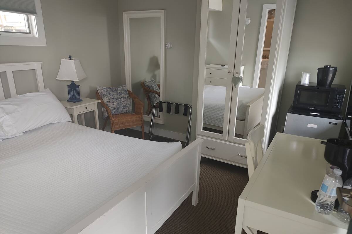 A hotel room with a bed, a chair, a desk, a microwave, and a water bottle.
