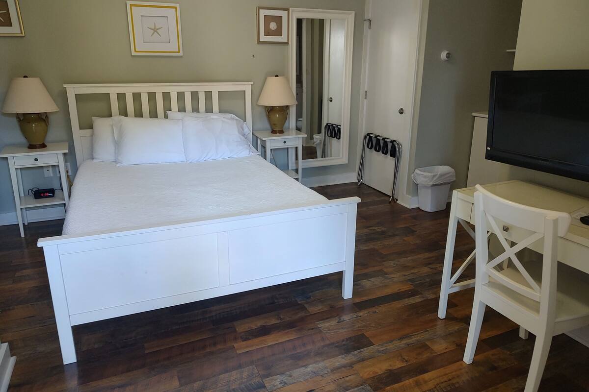 A bedroom with a white bed, bedside tables with lamps, a TV, and a mirror.
