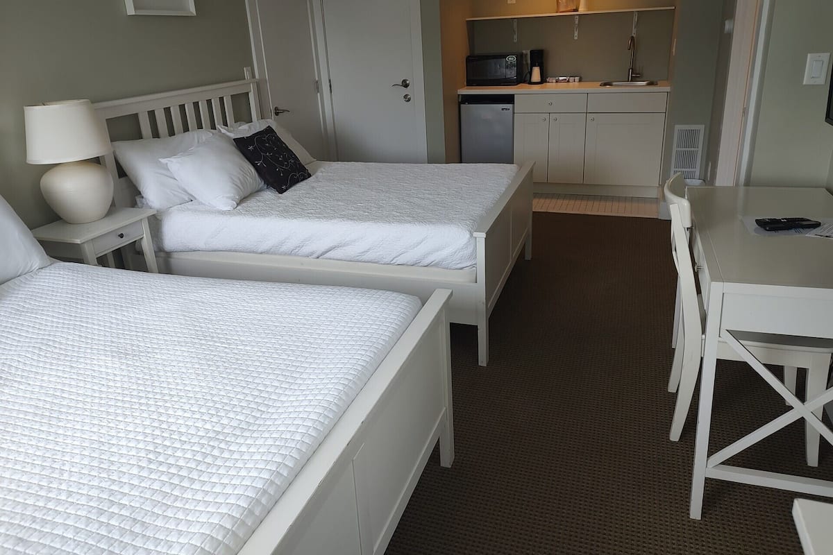 A hotel room with two beds, a small kitchenette, a dining table, and a white color scheme.
