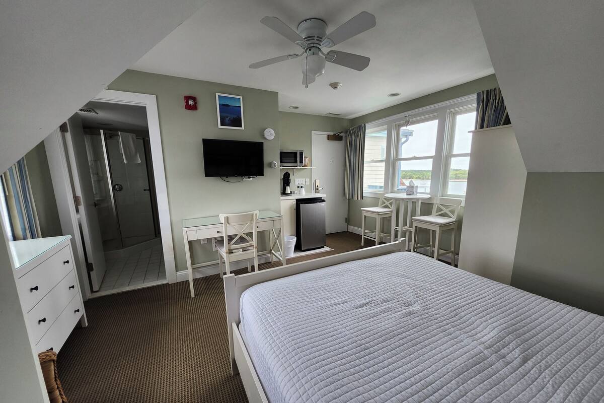 A hotel room with a bed, a desk, a chair, a TV, a microwave, and a window with a view.
