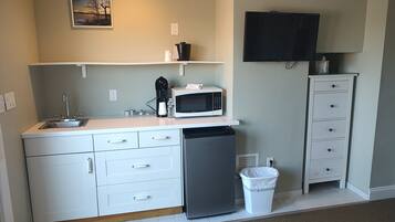 A compact kitchen with a sink, microwave, coffee maker, and a trash bin.