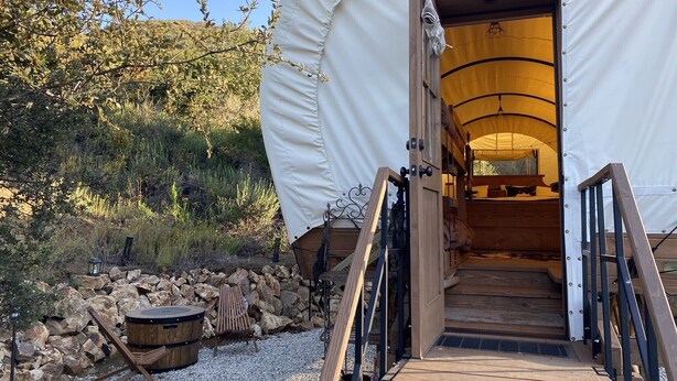 A tent with a wooden deck and a metal staircase leading to an interior with a bed and a table.