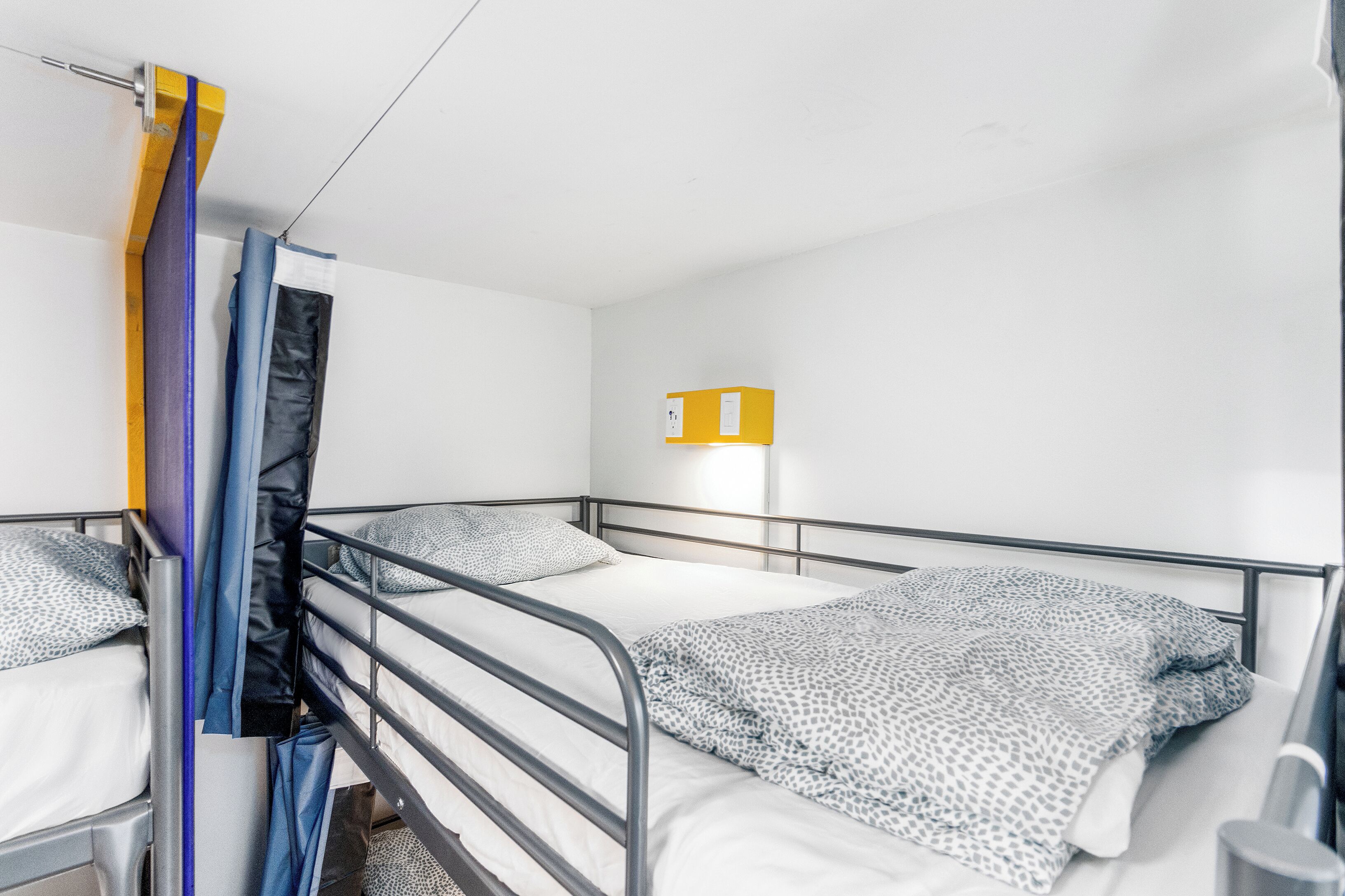 Habitación con literas de metal, una mesita pequeña y una lámpara fijada a la pared.