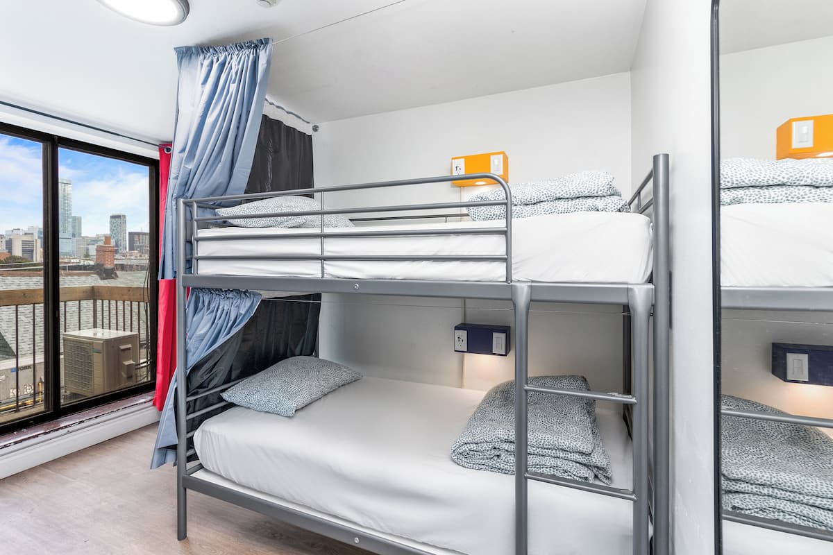 A bunk bed room with a city view, a window with curtains, and a wall-mounted light.
