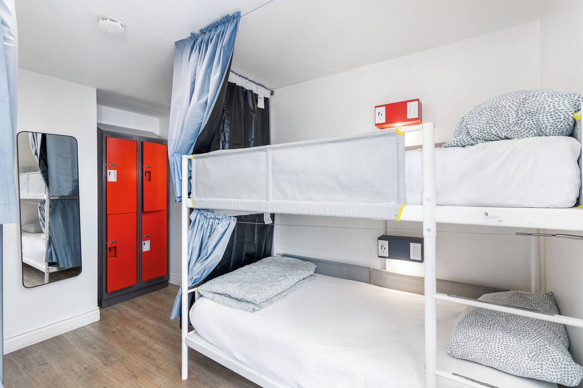 A bunk bed room with a mirror, red lockers, and a power outlet.