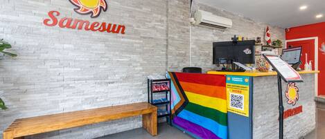 A reception area with a wooden bench, a counter with a rainbow flag, and a sign reading "Samesun".
