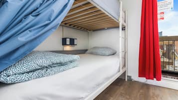A bunk bed with a headboard, a bedside table with a lamp, and a window with a red curtain.