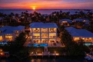 Une maison à plusieurs étages avec une piscine, entourée de palmiers et offrant une vue sur le coucher de soleil.