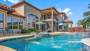 Una casa de dos pisos con piscina, mobiliario exterior y un patio cubierto.