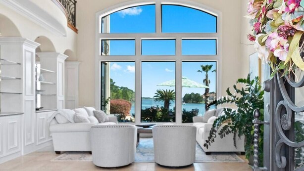 Amplia sala de estar con un gran ventanal de arco, mobiliario blanco y vista a un lago.