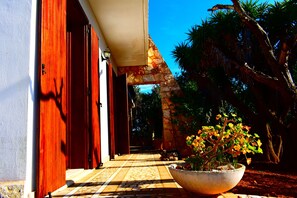 A pathway leading to a building with a red door, a stone archway, and a potted plant with yellow flowers. - Spacious villa surrounded by greenery, ideal for groups (many all-inclusive services) (Copertino)