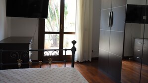 Ein Schlafzimmer mit Bett, Fernseher, Kleiderschrank und einem Fenster mit Vorhängen.