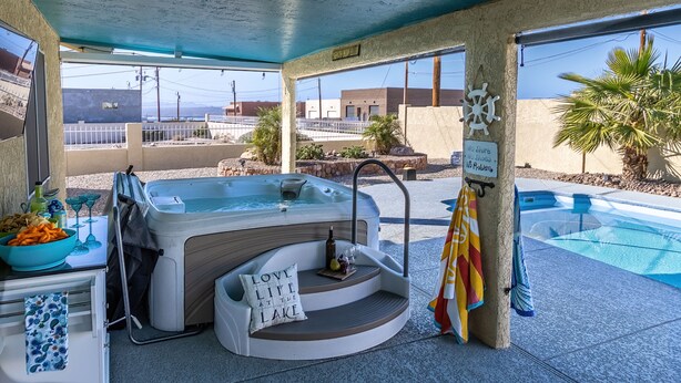 A hot tub with a sign reading "LOVE LIFE AT THE LAKE," a pool, and a view of buildings in the background.