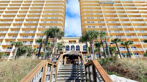 Ein Hotel mit einer zentralen Treppe, die zu einem überdachten Bereich führt, gesäumt von Palmen und einem Strand.