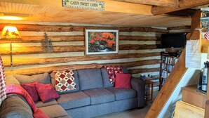 A cabin interior with a sofa, a lamp, a painting, and a bookshelf.
