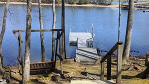 A wooden dock extending into a calm lake, surrounded by trees and a small dock structure.