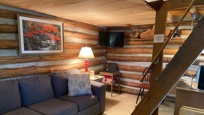 A log cabin interior with a sofa, a TV, a lamp, and a staircase.
