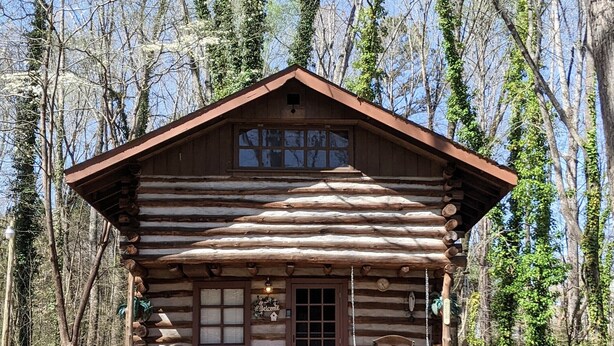 A log cabin with a porch, outdoor seating, and a welcome sign.