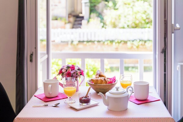 Een ontbijttafel met een witte mok, een glas sinaasappelsap, een schaal croissants, een theepot en een klein glaasje jam.
