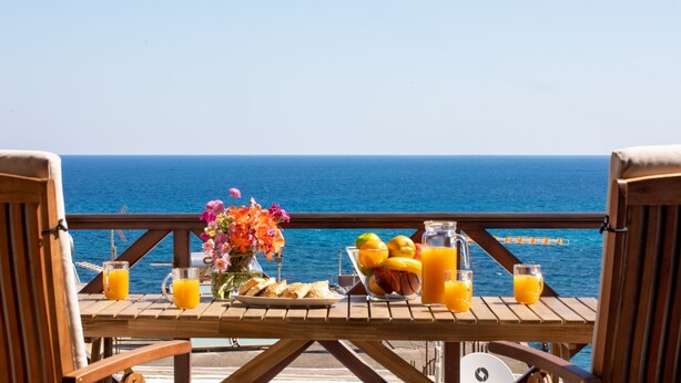 Une terrasse en bois avec une table mise pour le petit-déjeuner, offrant une vue sur l’océan.