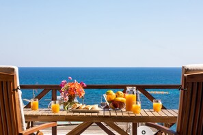 Une terrasse en bois avec une table mise pour le petit-déjeuner, offrant une vue sur l’océan.