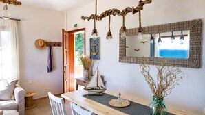 Un coin repas avec une table en bois, des chaises blanches, un vase contenant des plantes séchées, une petite maquette de voilier et un miroir agrémenté de lampes suspendues.