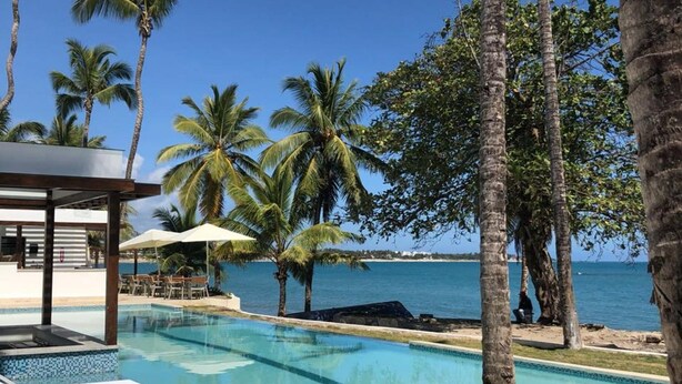 A pool area with lounge chairs, palm trees, and a view of the ocean.