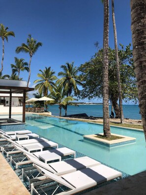 A pool area with lounge chairs, palm trees, and a view of the ocean. - 1 Bedroom Garden View Presidential Suites Cabarete (Sosúa)