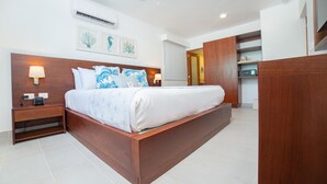 A modern hotel room with a large bed, wooden headboard, two bedside tables with lamps, an air conditioning unit, and a ceiling fan.