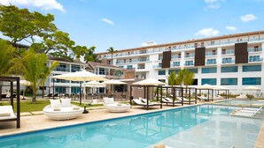 A pool area with lounge chairs and umbrellas, a modern building with multiple balconies, and a clear blue sky.