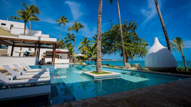 A pool area with lounge chairs, palm trees, and a view of the ocean.