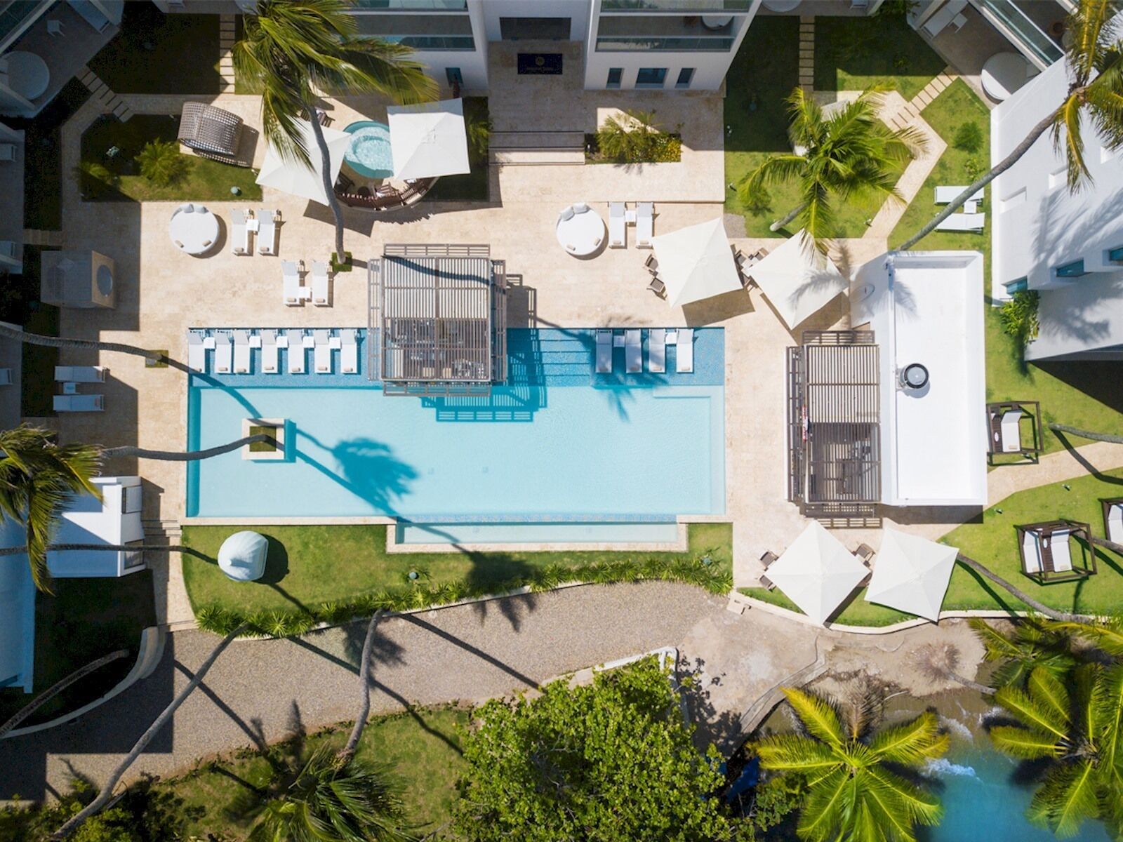 An aerial view of a resort with a central pool, sun loungers, and palm trees.