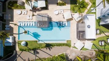 An aerial view of a resort with a central pool, sun loungers, and palm trees.