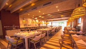 A spacious restaurant with multiple dining tables and chairs, warm lighting, and a brick wall on one side. - 1 Bedroom Garden View Presidential Suites Cabarete (Sosúa)