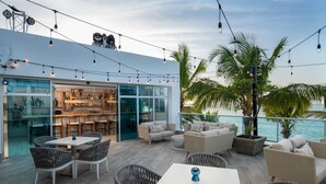 An outdoor seating area with wicker furniture, a bar with shelves of bottles, and a view of the ocean. - 1 Bedroom Garden View Presidential Suites Cabarete (Sosúa)