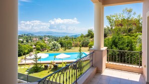 A balcony with a view of a swimming pool, lush greenery, and distant mountains. - Villa Denise in Corfu (Corfu)