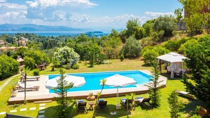 A swimming pool with a view of the sea and mountains, surrounded by greenery and outdoor seating. - Villa Denise in Corfu (Corfu)