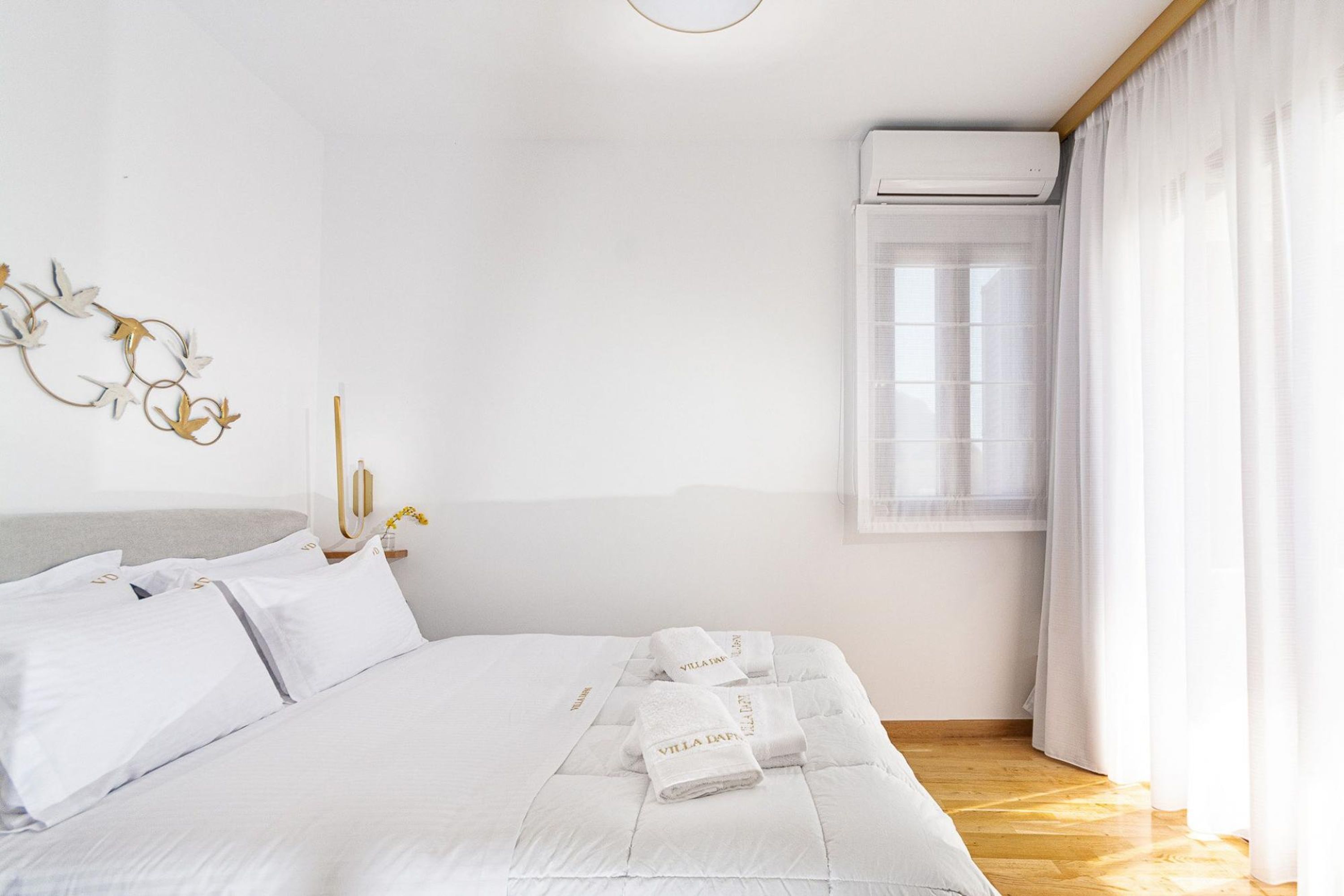 Ein Hotelzimmer mit einem Bett, weißer Bettwäsche, einer Wand-Klimaanlage und einem Fenster mit Vorhängen.