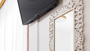 Una stanza con un comò in legno, una televisione fissata al muro e uno specchio decorativo con cornice bianca.