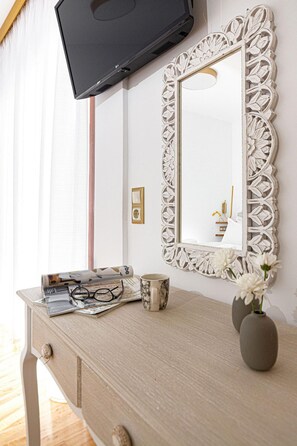 Une pièce comprenant une commode en bois, un téléviseur fixé au mur et un miroir décoratif doté d’un cadre blanc.