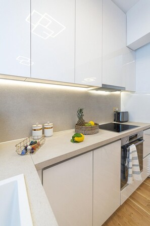 Una cocina moderna con armarios blancos, estufa integrada y una pequeña isla con un frutero.