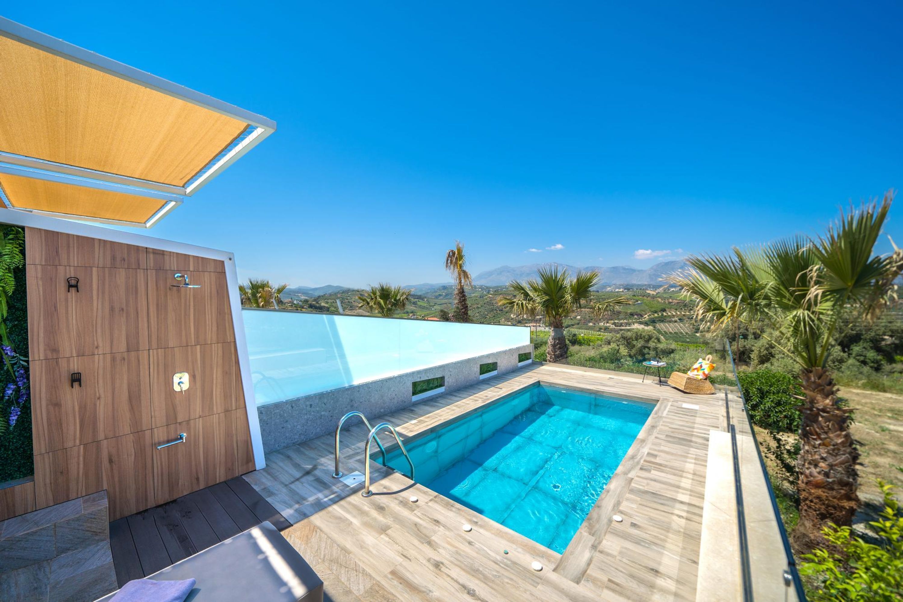 Un área de piscina exterior moderna con un muelle de madera, un cerramiento de vidrio y vistas al paisaje.