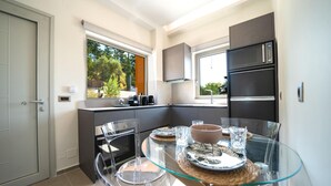 A modern kitchen with a glass dining table, stainless steel appliances, and a view of greenery outside.
