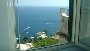 A view through a window of a coastal area with boats on the water, buildings, and greenery.
