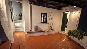 A covered outdoor area with a wooden floor, a small window with shutters, and a green door. - When an overlook becomes poetry (Amalfi)
